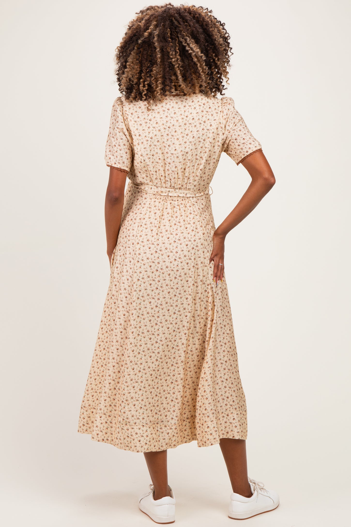 woman wearing a beige floral maternity dress with short sleeves and a waist tie, showing her back