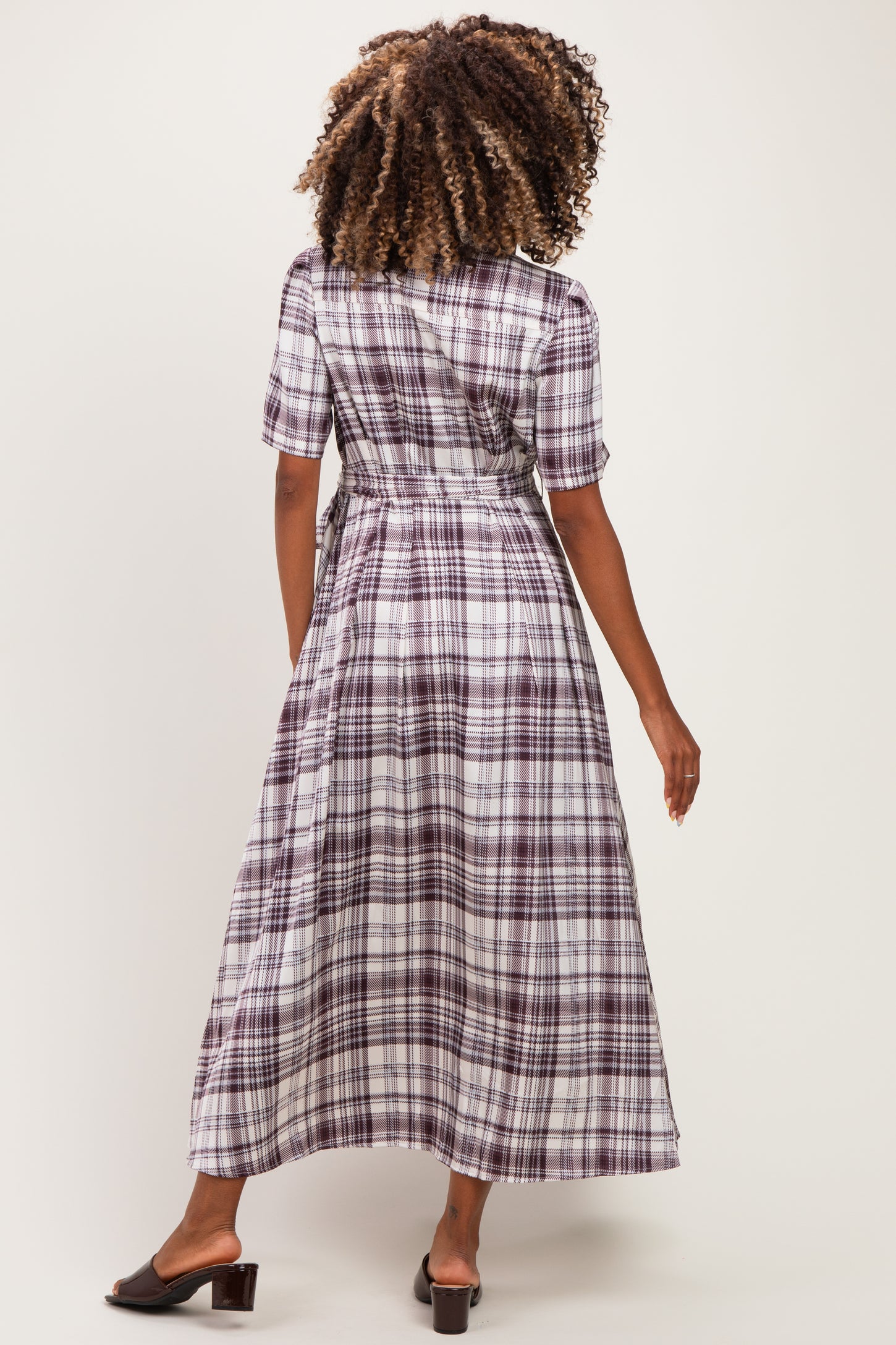 woman wearing a long purple plaid maternity dress, showing the back view with a fitted waist and short sleeves
