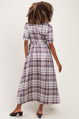woman wearing a long purple plaid maternity dress, showing the back view with a fitted waist and short sleeves