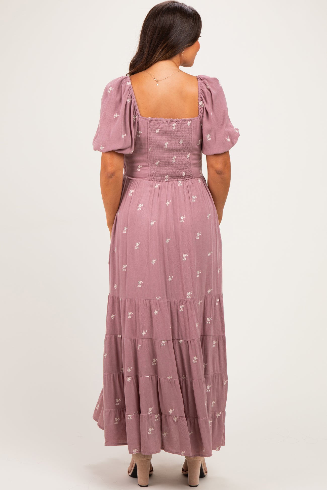 woman wearing a dusty pink maternity maxi dress with puff sleeves and floral embroidery, showing her baby bump from the back