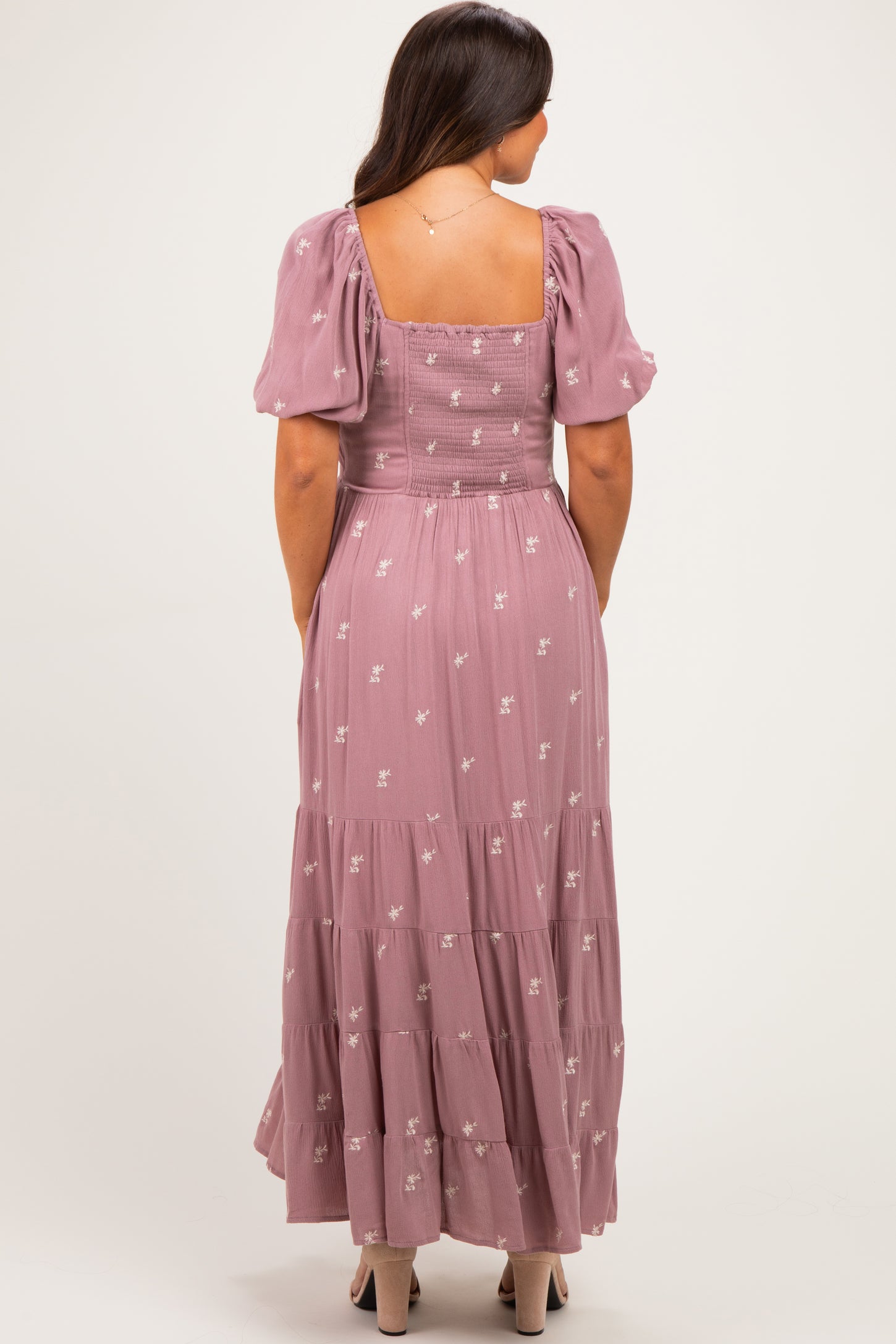woman wearing a dusty pink maternity maxi dress with puff sleeves and floral embroidery, showing her baby bump from the back