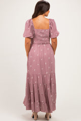 woman wearing a dusty pink maternity maxi dress with puff sleeves and floral embroidery, showing her baby bump from the back