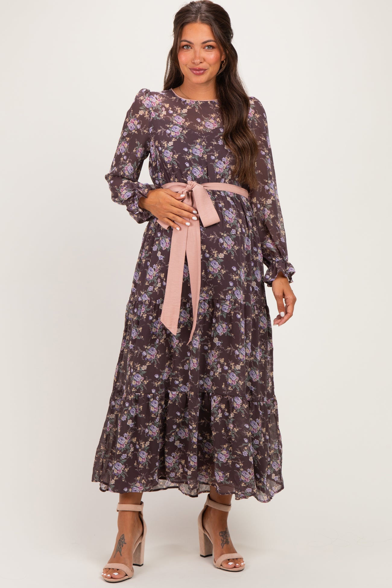 woman wearing a long sleeve dark floral maternity dress with a pink tie waist detail and a flowing skirt