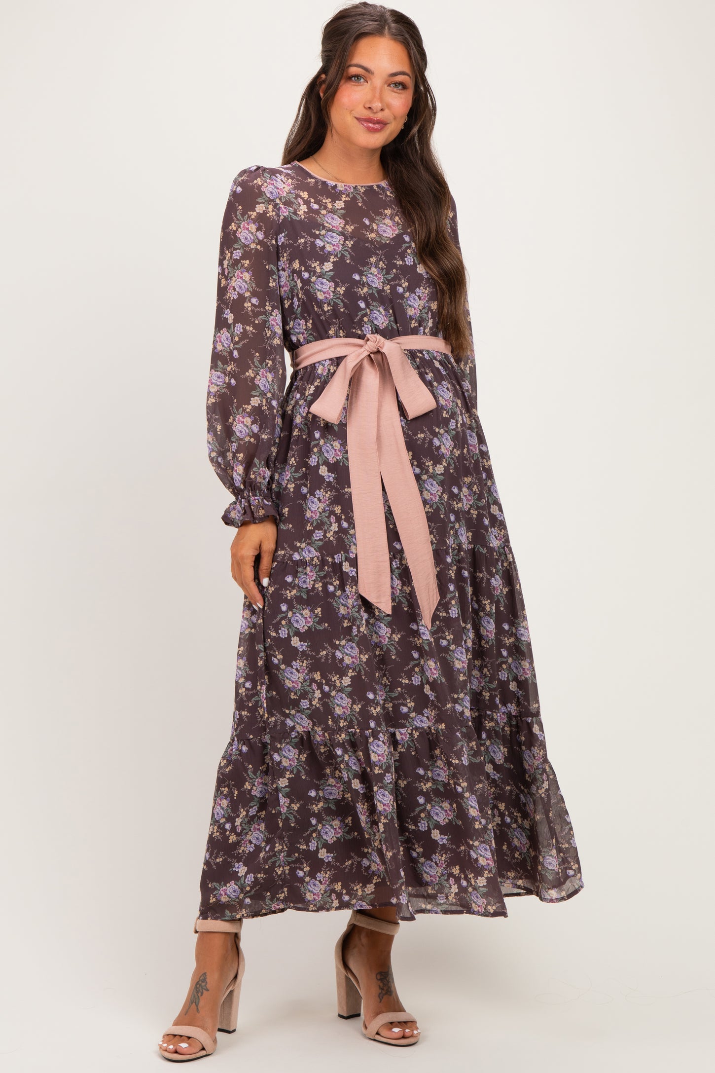woman wearing a dark floral maternity dress with long sleeves and a pink ribbon belt, showcasing a baby bump