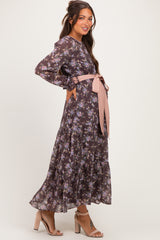 woman wearing a dark floral maternity dress with long sleeves and a tied waist detail, showcasing her baby bump