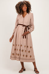 woman wearing a beige maternity dress with floral embroidery and long sleeves, styled with a brown belt