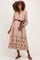 woman wearing a beige maternity dress with floral embroidery and long sleeves, styled with a brown belt