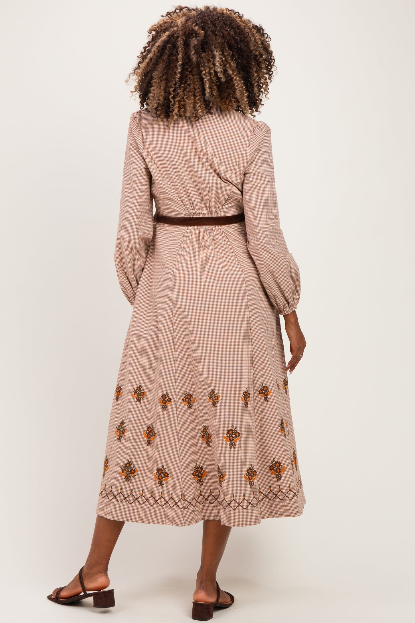 woman wearing a striped maternity dress with floral embroidery and long sleeves, styled with a brown belt, showing back view