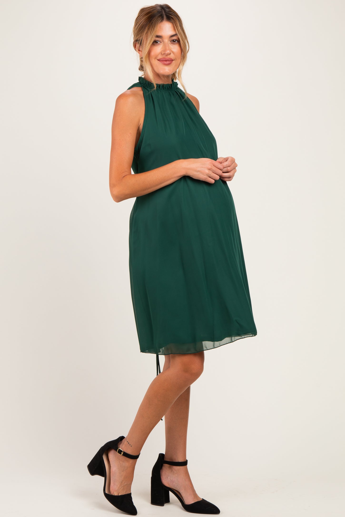 woman wearing a dark green halter neck maternity dress with a flowy silhouette and visible baby bump