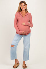 woman wearing a rose pink maternity hoodie and light blue distressed maternity jeans, holding her baby bump