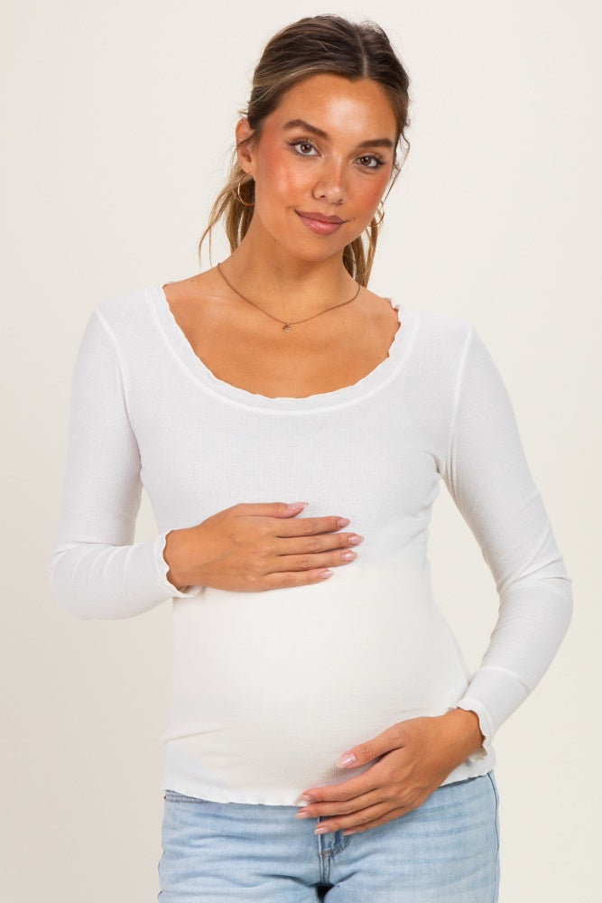 woman wearing a white long sleeve maternity top with a scoop neckline and holding her baby bump