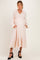 woman wearing a blush pink maternity dress with a smocked bodice and long sleeves, featuring a tiered skirt and pockets