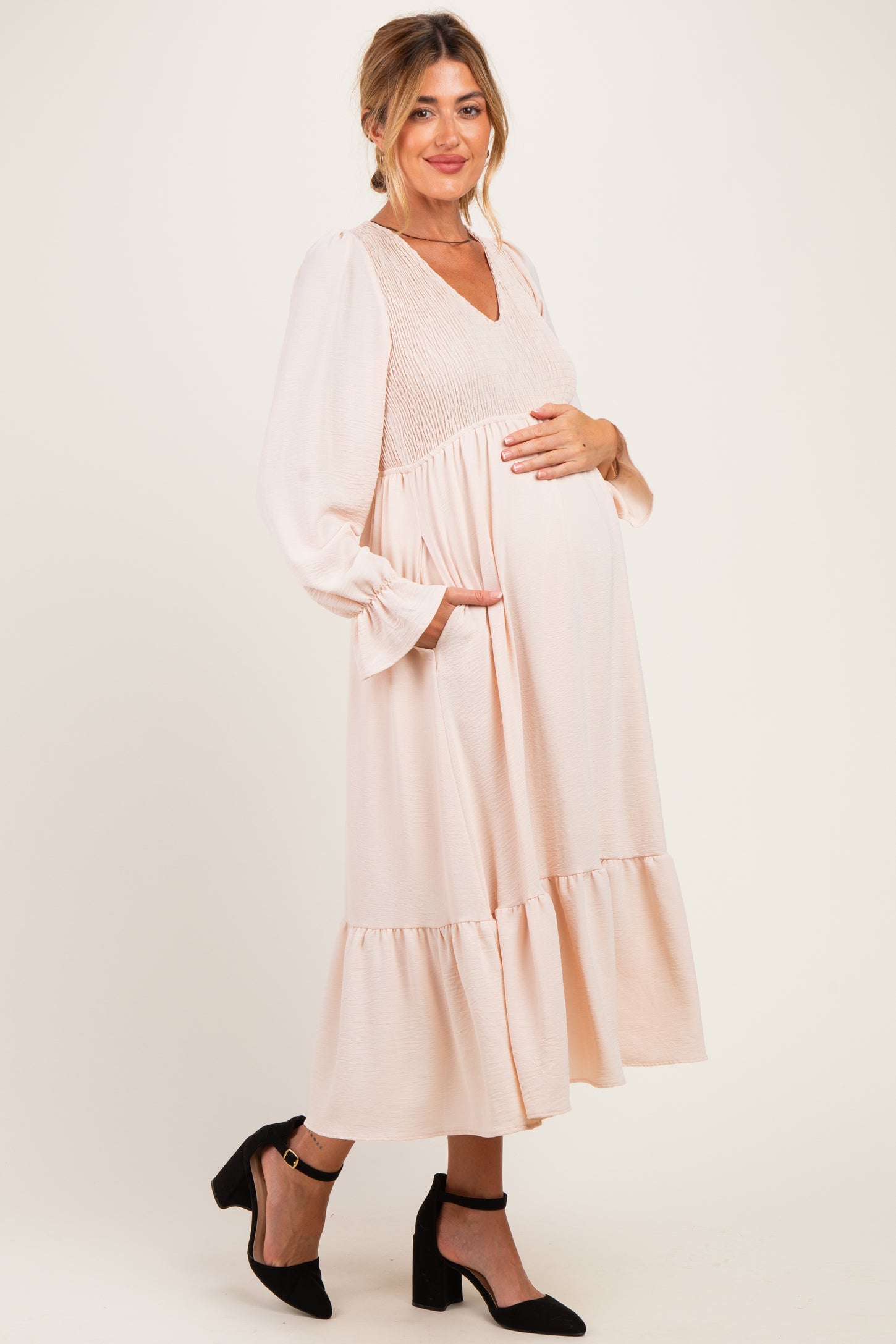 woman wearing a light pink maternity dress with a smocked bodice and tiered skirt, holding her baby bump