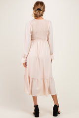 woman wearing a back view of a light pink maternity dress with smocked bodice and long sleeves