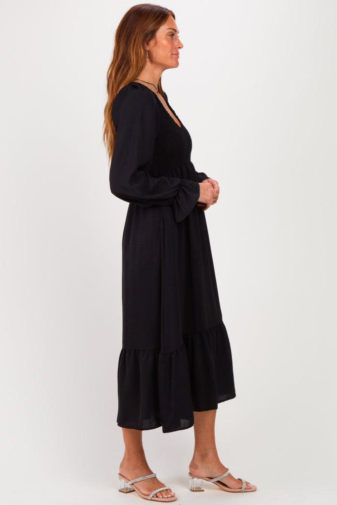 woman wearing a black long sleeve dress with a smocked bodice and tiered hem, standing in profile