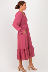 woman wearing a pink smocked midi dress with long sleeves and ruffled hem, styled with neutral sandals