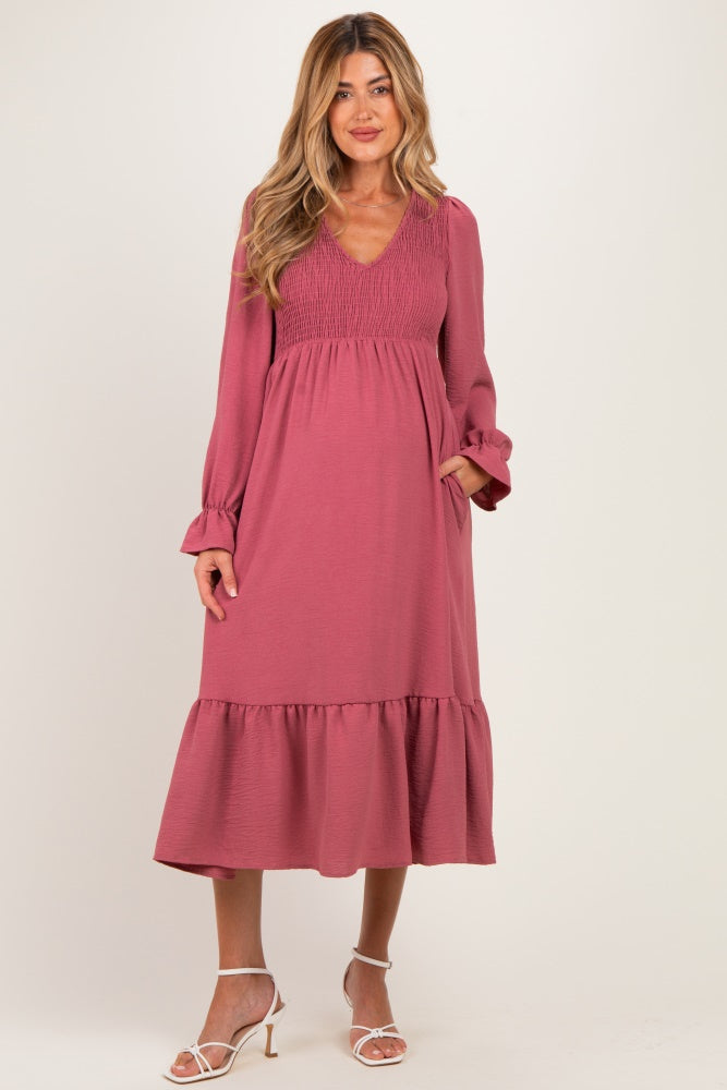 woman wearing a dusty rose maternity dress with a smocked bodice and ruffle hem, holding her baby bump