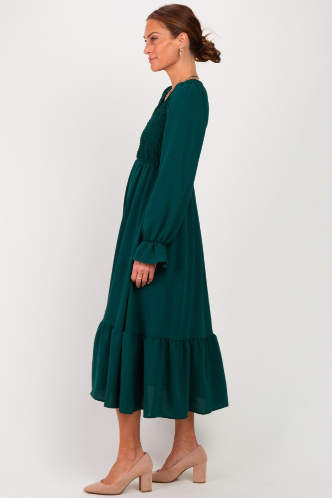 woman wearing a dark green long sleeve maxi dress with smocked bodice and ruffled hem, styled with nude heels