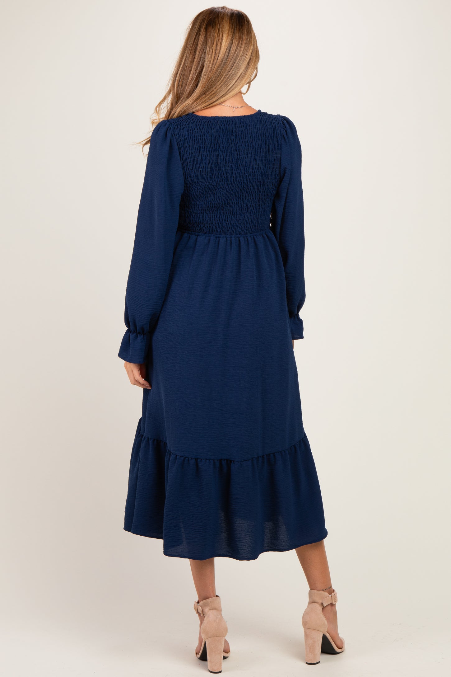 woman wearing a navy blue maternity dress with long sleeves and a tiered skirt, showing a smocked back detail