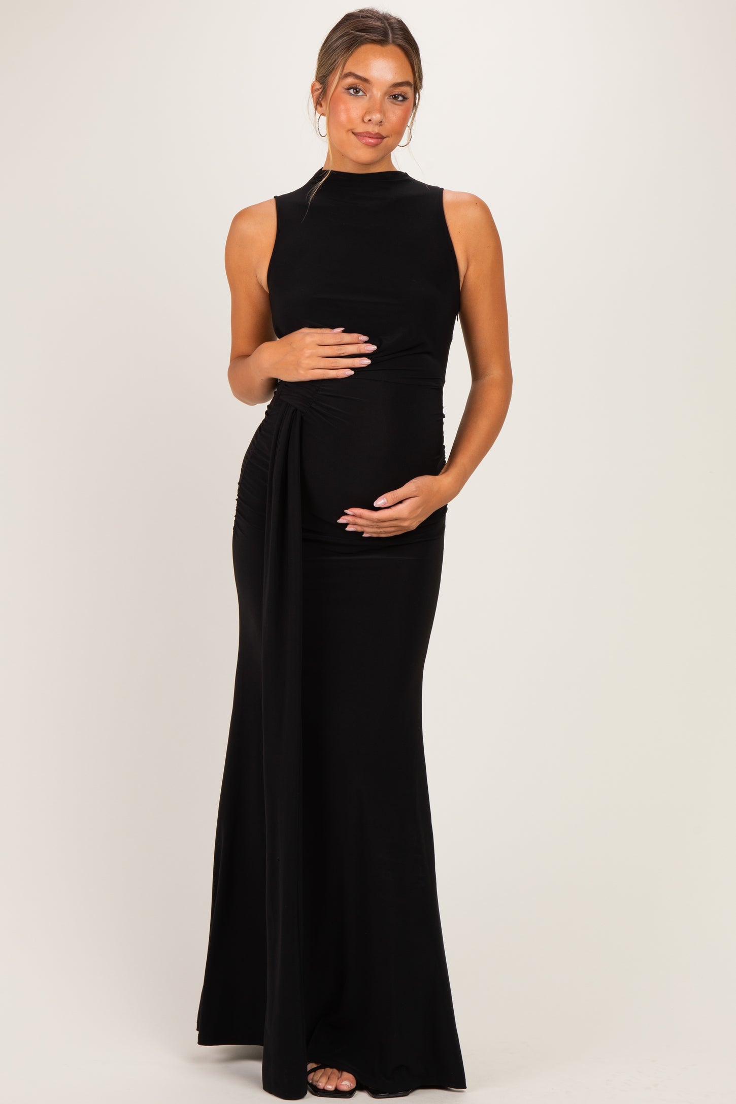 woman wearing a black sleeveless maternity dress with side ruching, holding her baby bump
