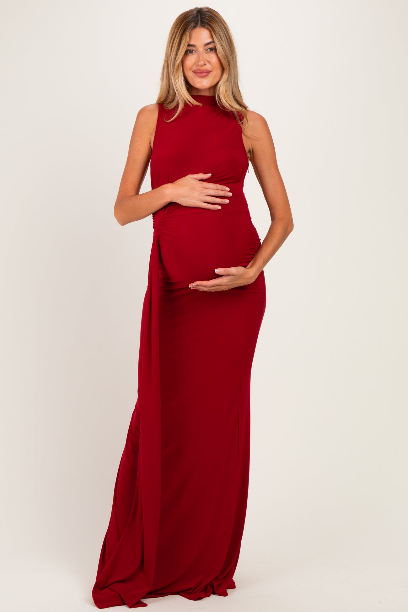 woman wearing a red sleeveless maternity gown with ruching, displaying her baby bump