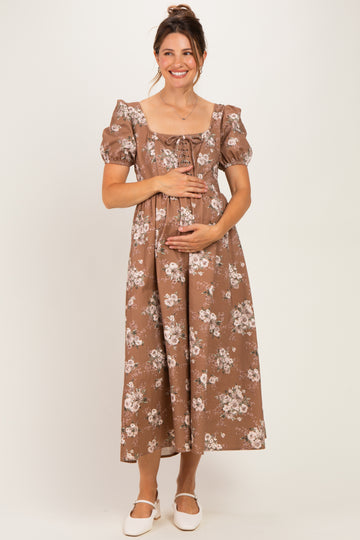 woman wearing a brown floral maternity dress with puff sleeves and a lace-up front, holding her baby bump