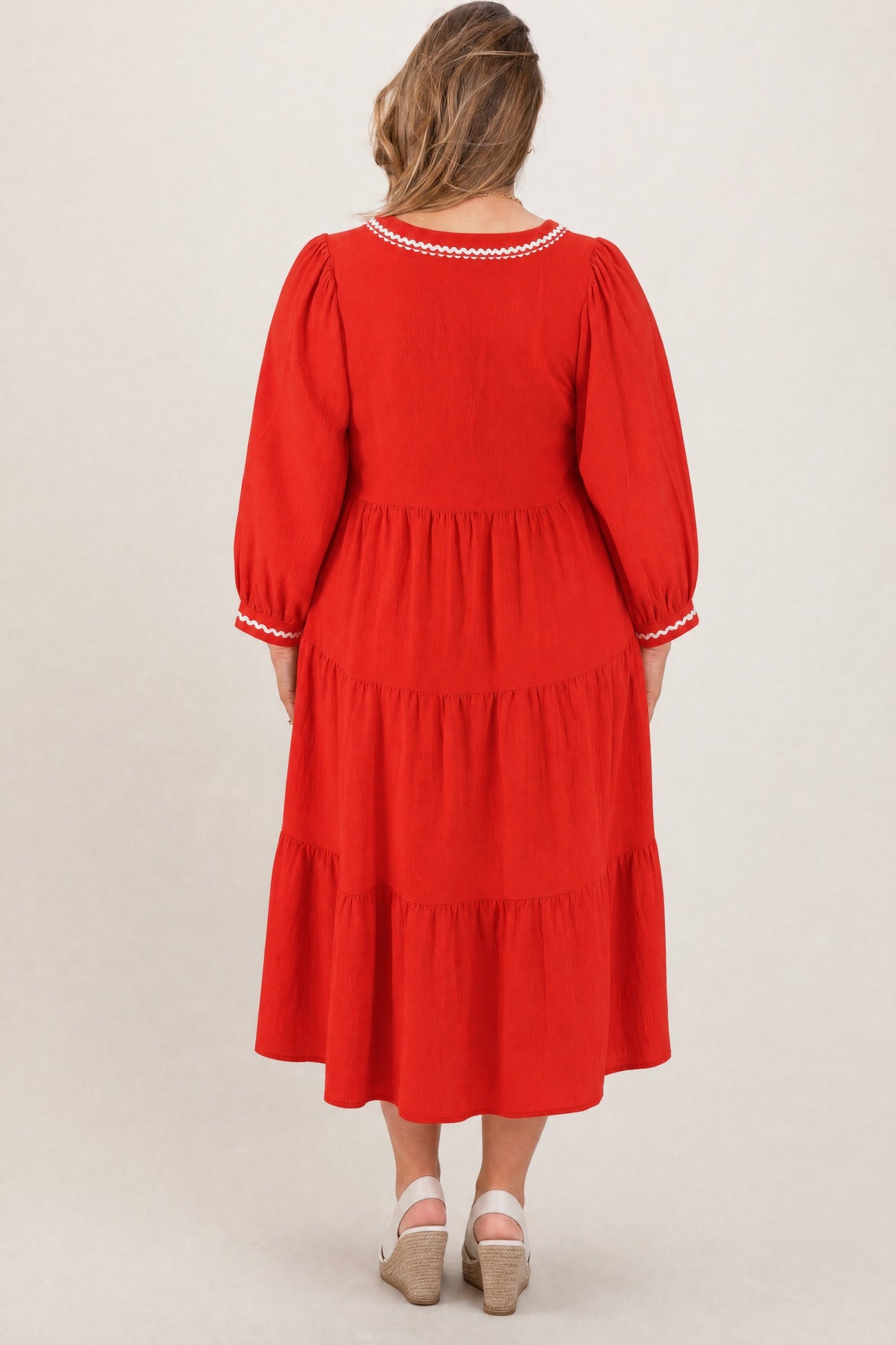 woman wearing a red maternity plus dress with three tiers and puff sleeves, seen from the back