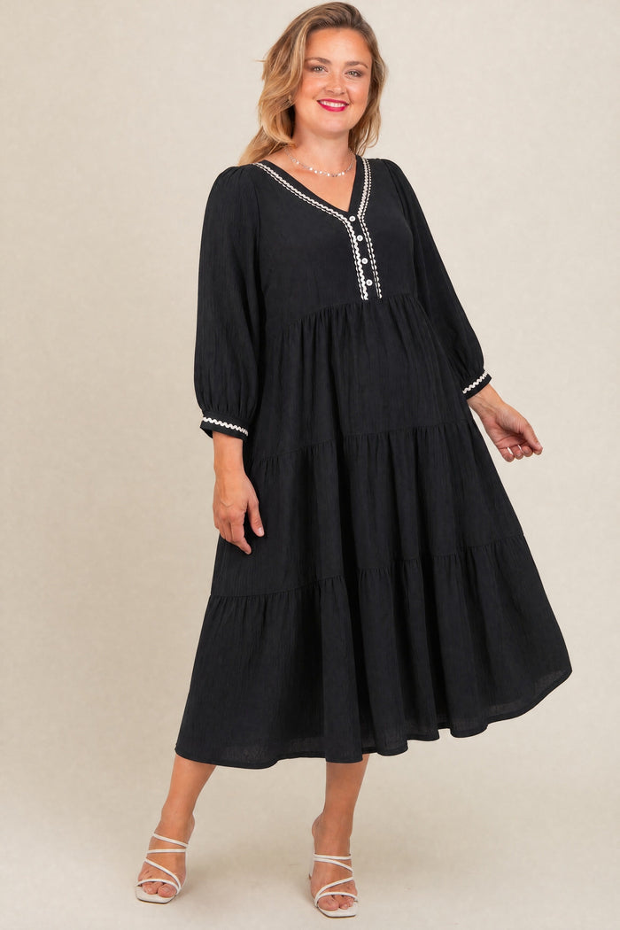woman wearing a black maternity plus tiered dress with balloon sleeves and decorative buttons