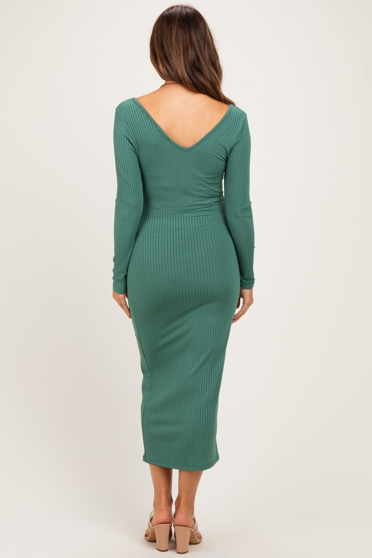 woman wearing a dark green ribbed maternity dress with a v-back and long sleeves, showing her baby bump
