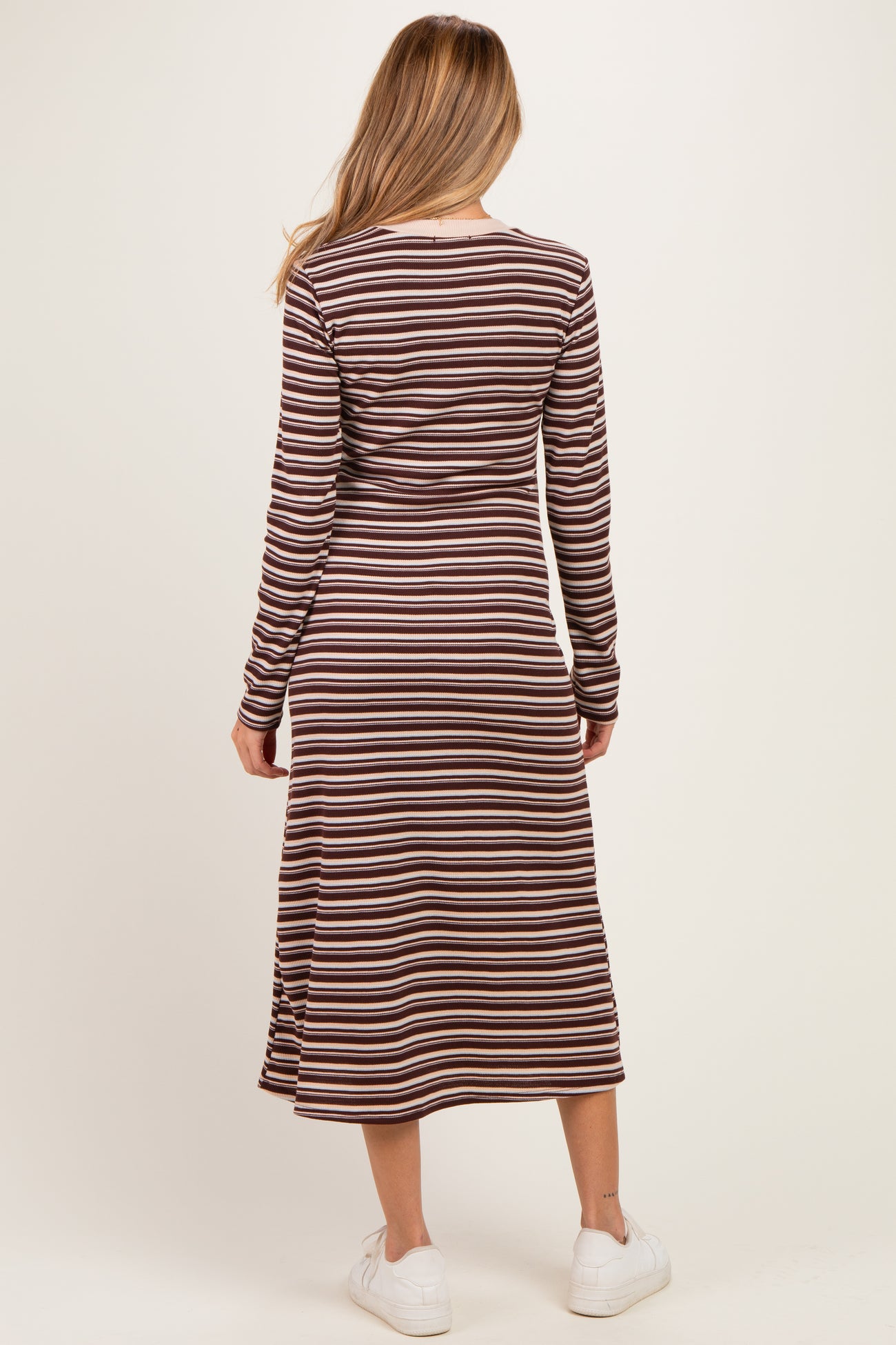 woman wearing a long sleeve brown and cream striped maternity dress with a midi length and side slits