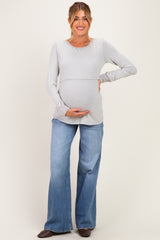 woman wearing a light gray long sleeve maternity top and blue flared jeans, holding her baby bump