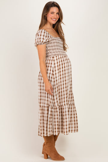 woman wearing a brown and white checked maternity dress with a smocked bodice and tiered skirt, showing her baby bump