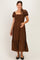 woman wearing a brown plaid maternity maxi dress with puff sleeves and a tiered hem, smiling and holding her baby bump