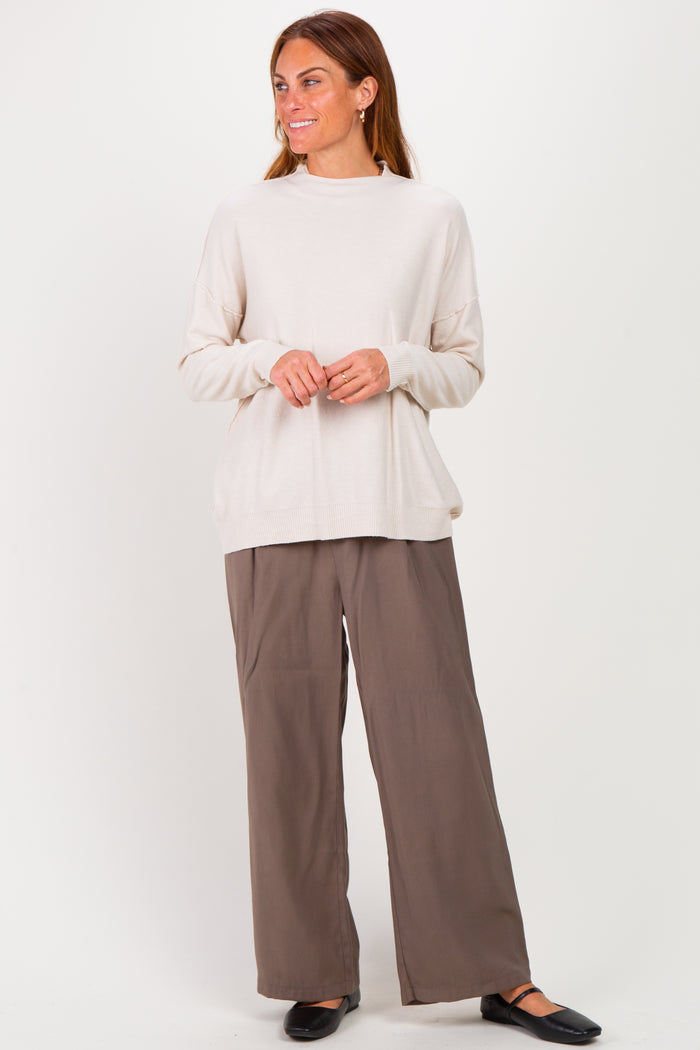 woman wearing a cream oversized sweater and brown wide-leg pants, standing with a relaxed pose