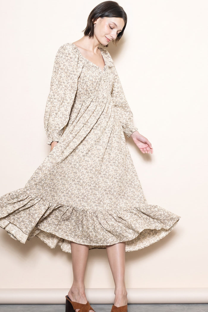 woman wearing a beige floral long sleeve dress with a ruffled hem and a v-neckline