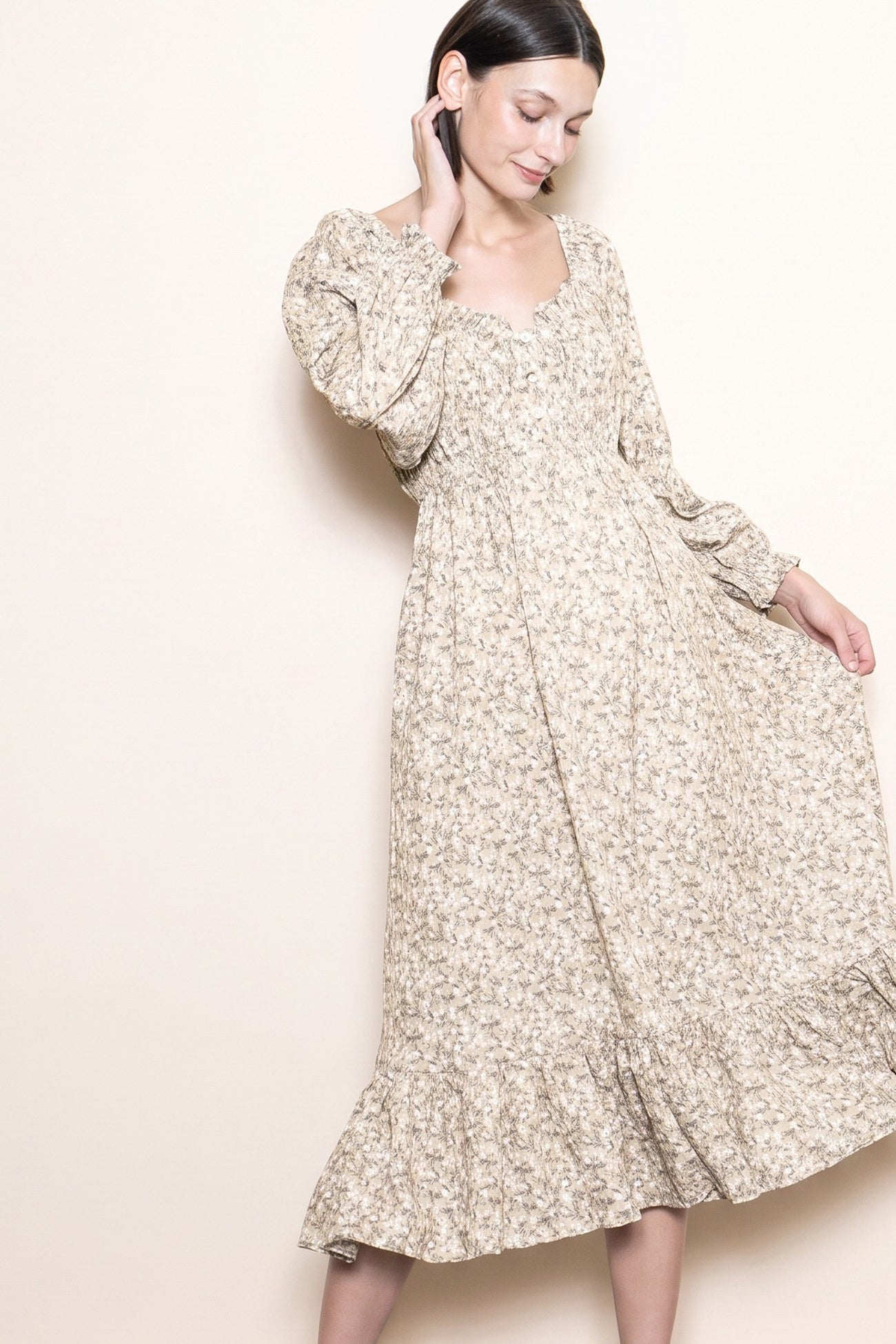 woman wearing a beige floral midi dress with long puff sleeves and a ruffled hem, posing against a neutral background