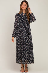 woman wearing a floral black maternity maxi dress with long sleeves and a tied neckline, showing her baby bump