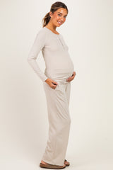 woman wearing a light taupe maternity long sleeve top and matching pants, cradling her baby bump