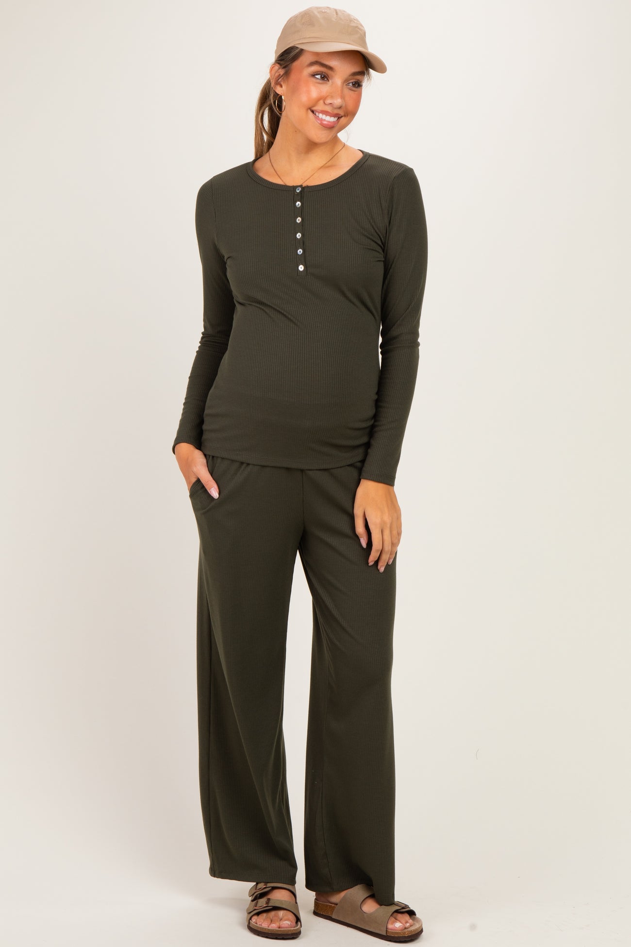 woman wearing a dark green long sleeve maternity top and matching pants, showcasing her baby bump