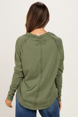 woman wearing an olive green long sleeve maternity top with distressed detailing and a relaxed fit