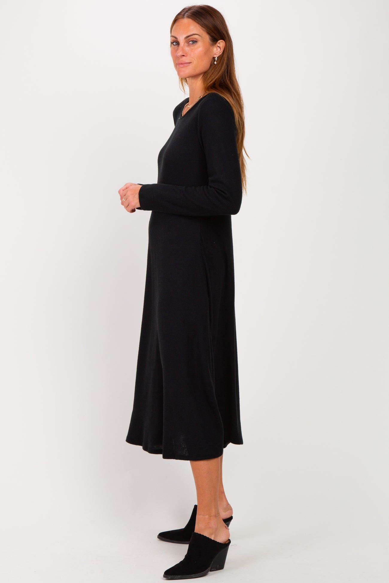 woman wearing a long black ribbed dress with a v-neck and a flared hem, standing sideways