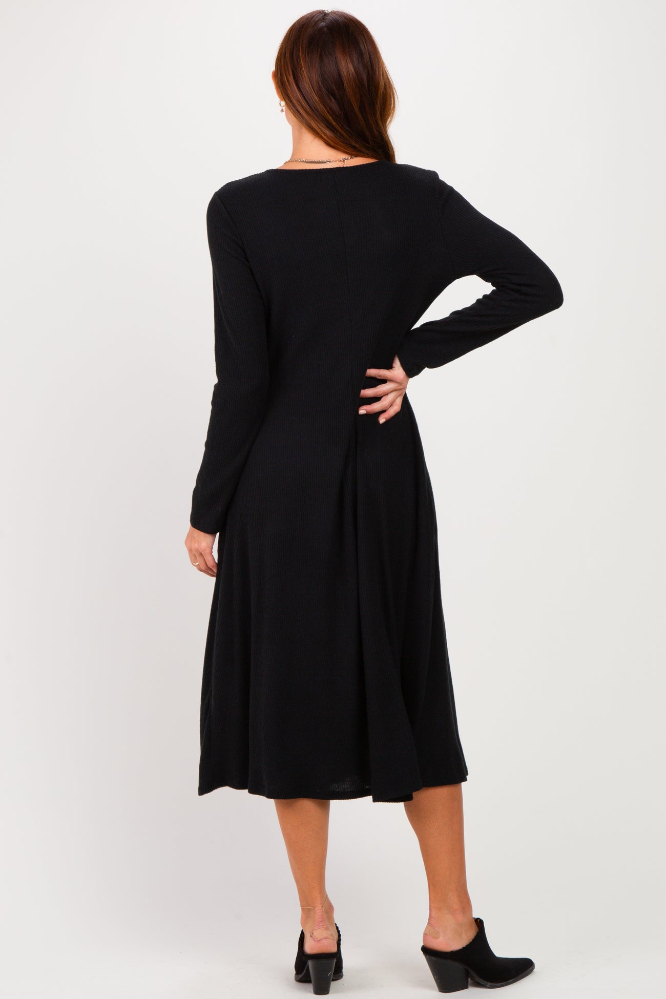 woman wearing a black long sleeve midi dress with a pleated back detail and heeled mules