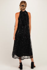 woman wearing a black maternity dress with a halter neck and flowing overlay, featuring intricate detailing at the hem