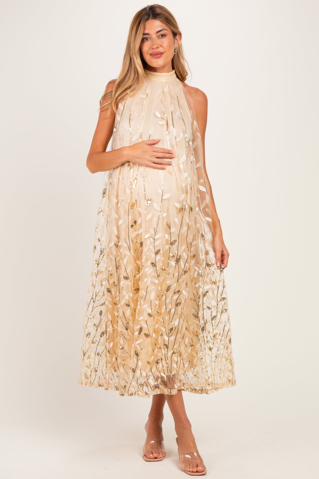 woman wearing a flowy beige maternity dress with floral embroidery, gently cradling her baby bump