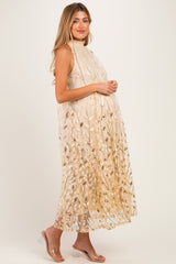 woman wearing a cream maternity dress with gold floral details and a flowing silhouette, showcasing her baby bump