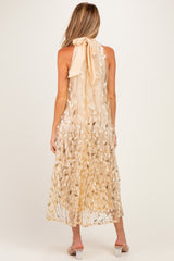 woman wearing a sheer beige maternity maxi dress with leaf patterns and a halter neck tie, showing her baby bump