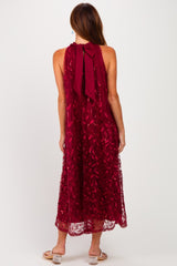 woman wearing a burgundy sleeveless maxi dress with a leafy embroidered design and a bow tie detail at the back