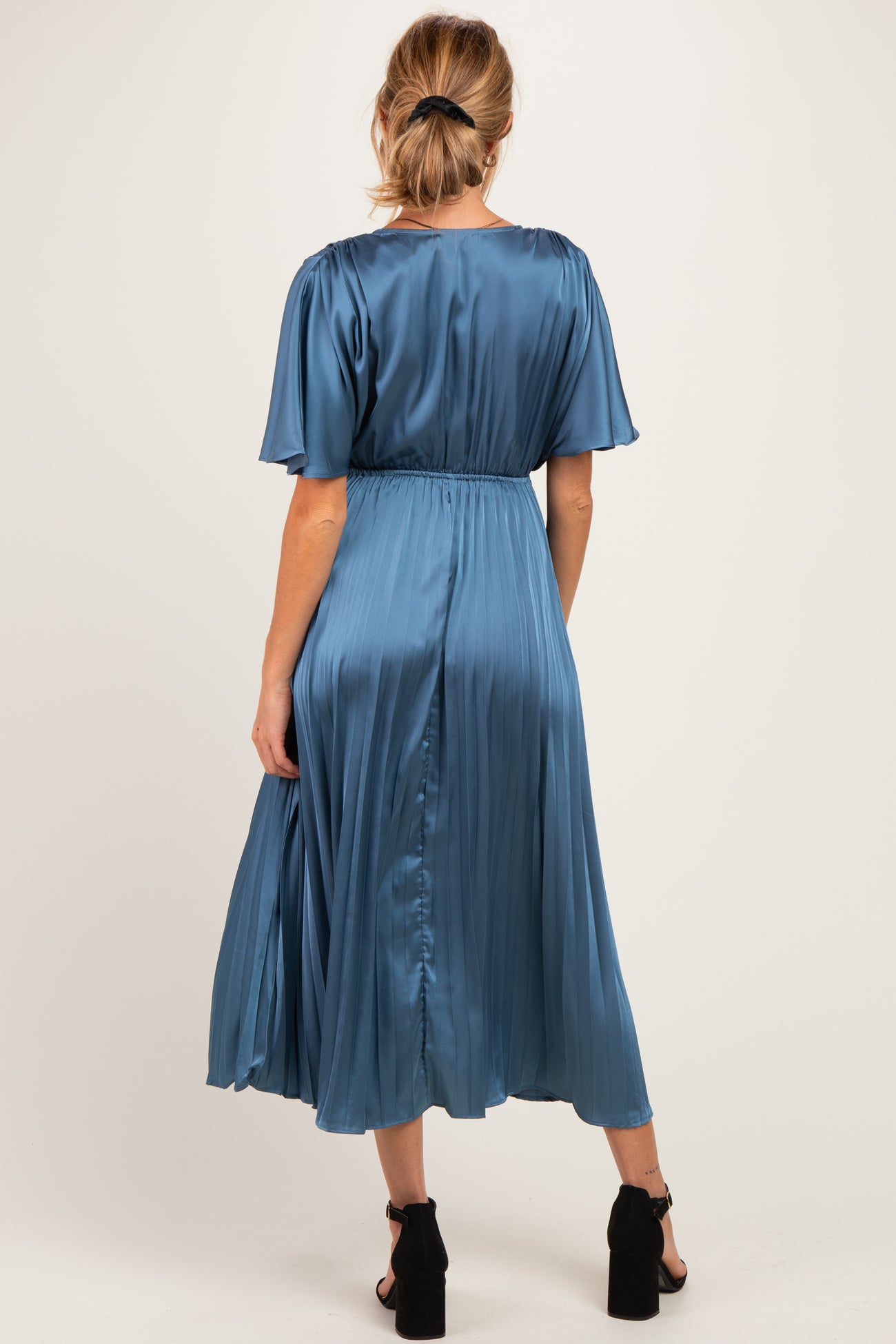 woman wearing a blue satin maternity maxi dress with flutter sleeves and a cinched waist, showing a baby bump