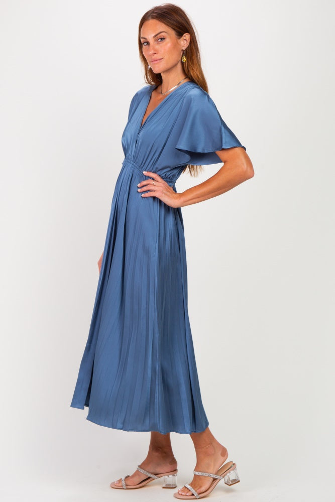 woman wearing a blue pleated maxi dress with short sleeves and a cinched waist, paired with silver sandals