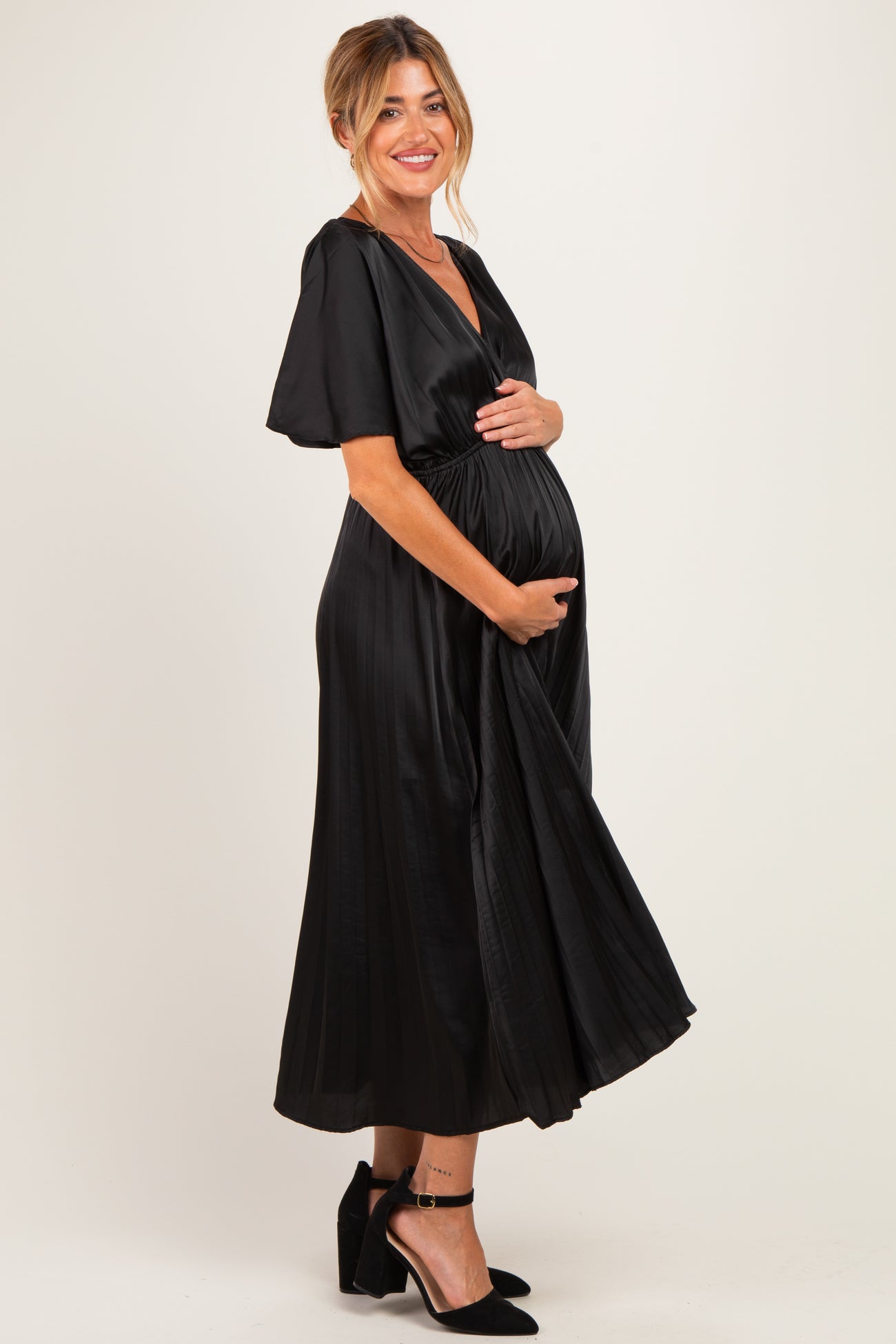 woman wearing a black satin maternity dress with short sleeves and a tied waist, holding her baby bump